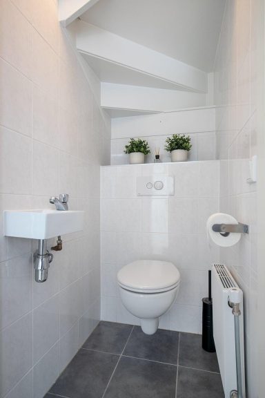 Toilet renovatie in Waalwijk Een moderne, kleine toiletruimte met toilet, fonteintje en handdoekrail.