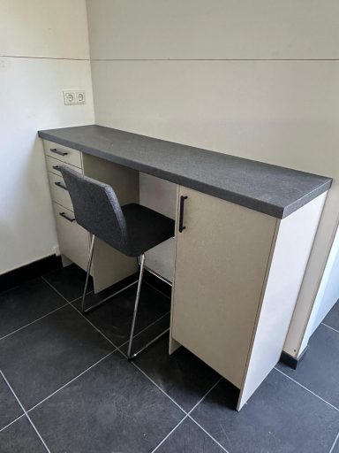 Een moderne bureau met een stoel en lade, tegen een lichte wand geplaatst.