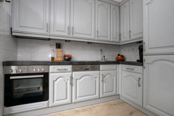 Keuken renovatie in Waalwijk Moderne keuken met grijze kasten, een oven en werkblad van graniet.