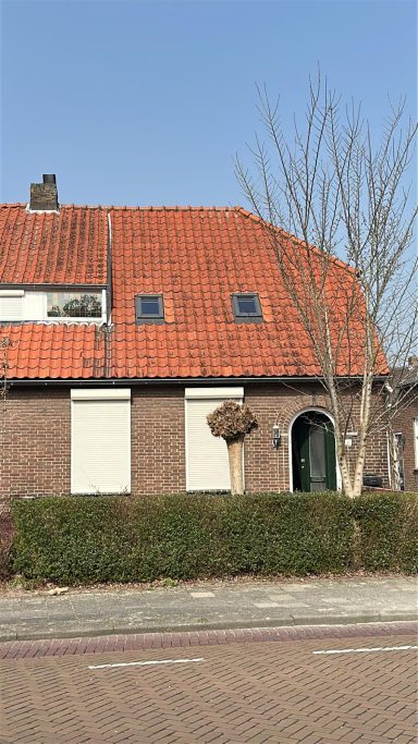 Velux dakramen in Vlijmen Een huis met een rood pannendak, groene deur en strakke schutting, onder een blauwe lucht.