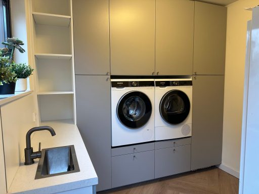 Bijkeuken in Rosmalen Wasmachine en droger naast een gootsteen in een moderne, neutraal ingerichte wasruimte.