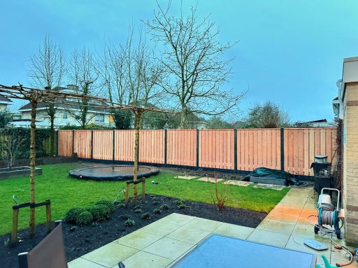 Hout-betonpaalschutting in Engelen Tuin met houten schutting, gras, een ronde vlonder en een patio.