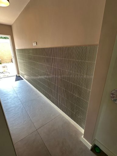 Lichte gang met een wand betegeld in een diagonaal patroon en een deur naar buiten.