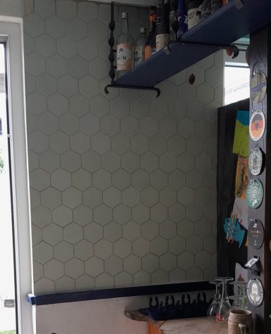 Wandtegels in 's-Hertogenbosch Moderne keuken met hexagonale tegels en een blauwe plank, gevuld met flessen.