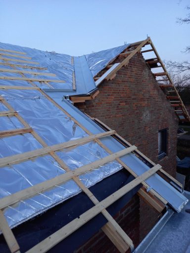 Dak renovatie in Maliskamp Dakconstructie met houten regels en metalen goot, onder een heldere lucht.