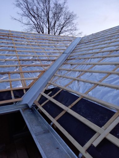 Dak renovatie in Maliskamp Dakconstructie met houten regels en metalen goot, onder een heldere lucht.