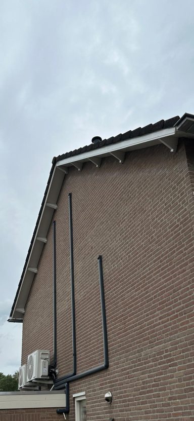 Dak renovatie in Berghem Hoek van een huis met een grijze lucht en zichtbare leidingen aan de gevel.