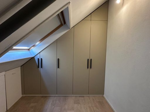 Kamer met schuine wand en ingebouwde kast met handgrepen, lichtinval vanuit het dakraam.